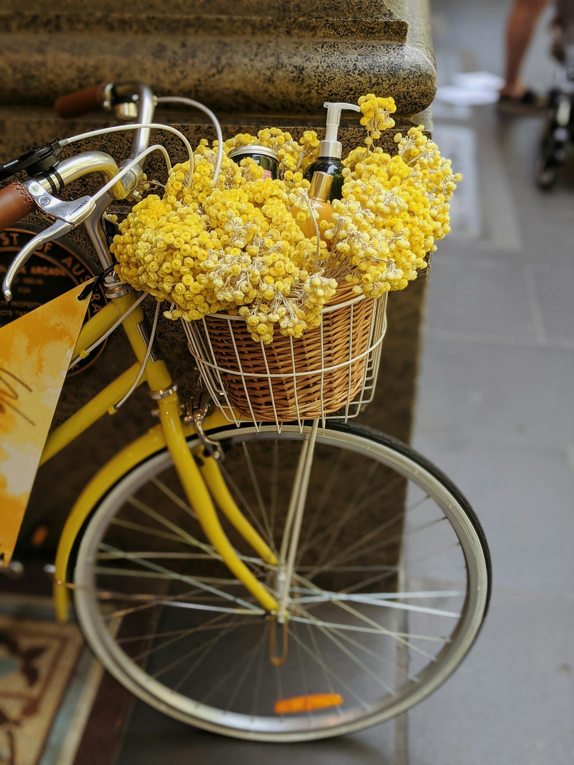 A vintage yellow bicycle adorned with a basket of vibrant yellow flowers on a Melbourne street.